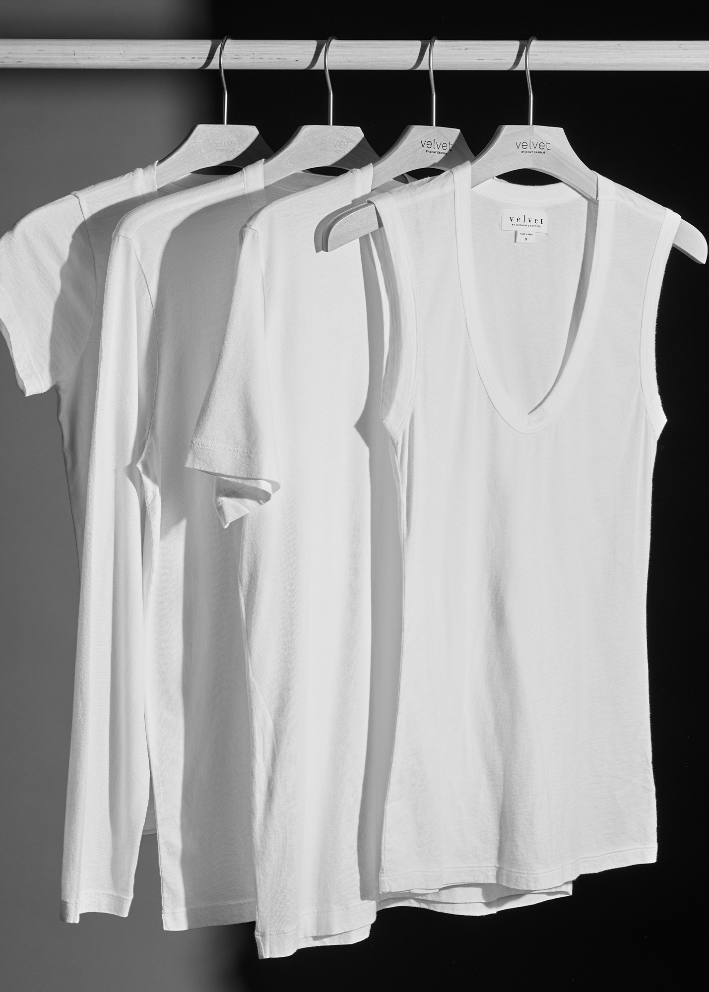 Four white shirts hanging on a rail against a white background.