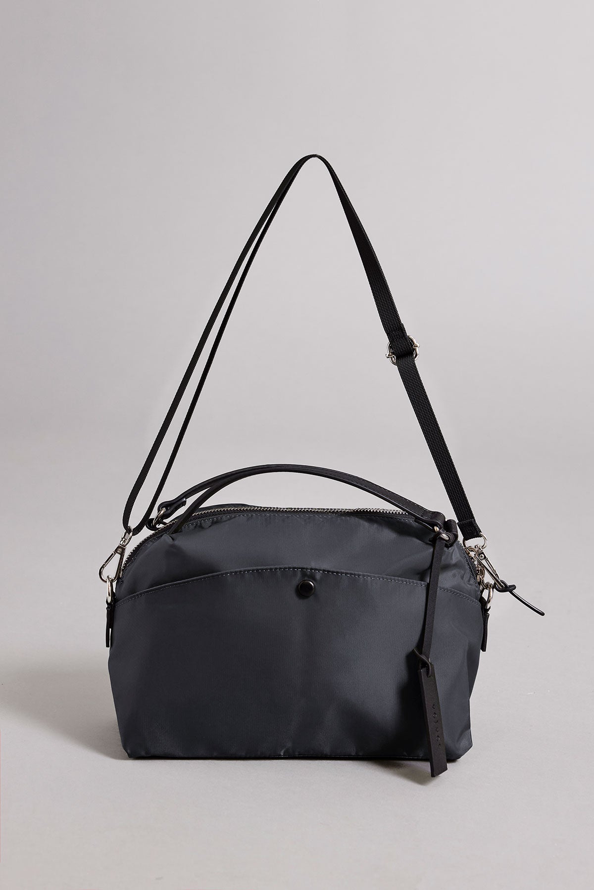 The NYLON CROSSBODY BAG by Velvet by Graham & Spencer is a black rectangular nylon shoulder bag with a front pocket, top zipper, adjustable strap, and small tag—perfect for everyday use and shown against a neutral background.