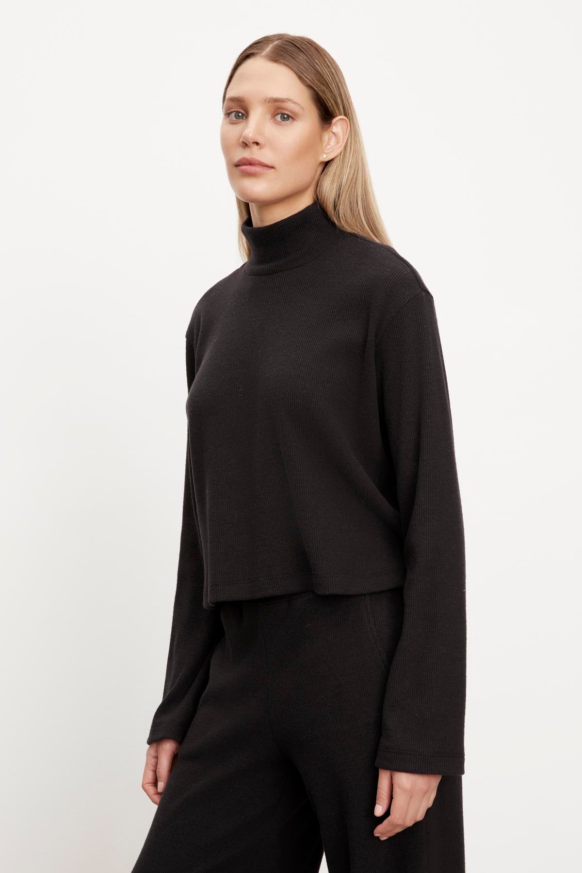 A model in a black ALEC BRUSHED RIB MOCK NECK TOP and wide leg pants by Velvet by Graham & Spencer.-35701823504577