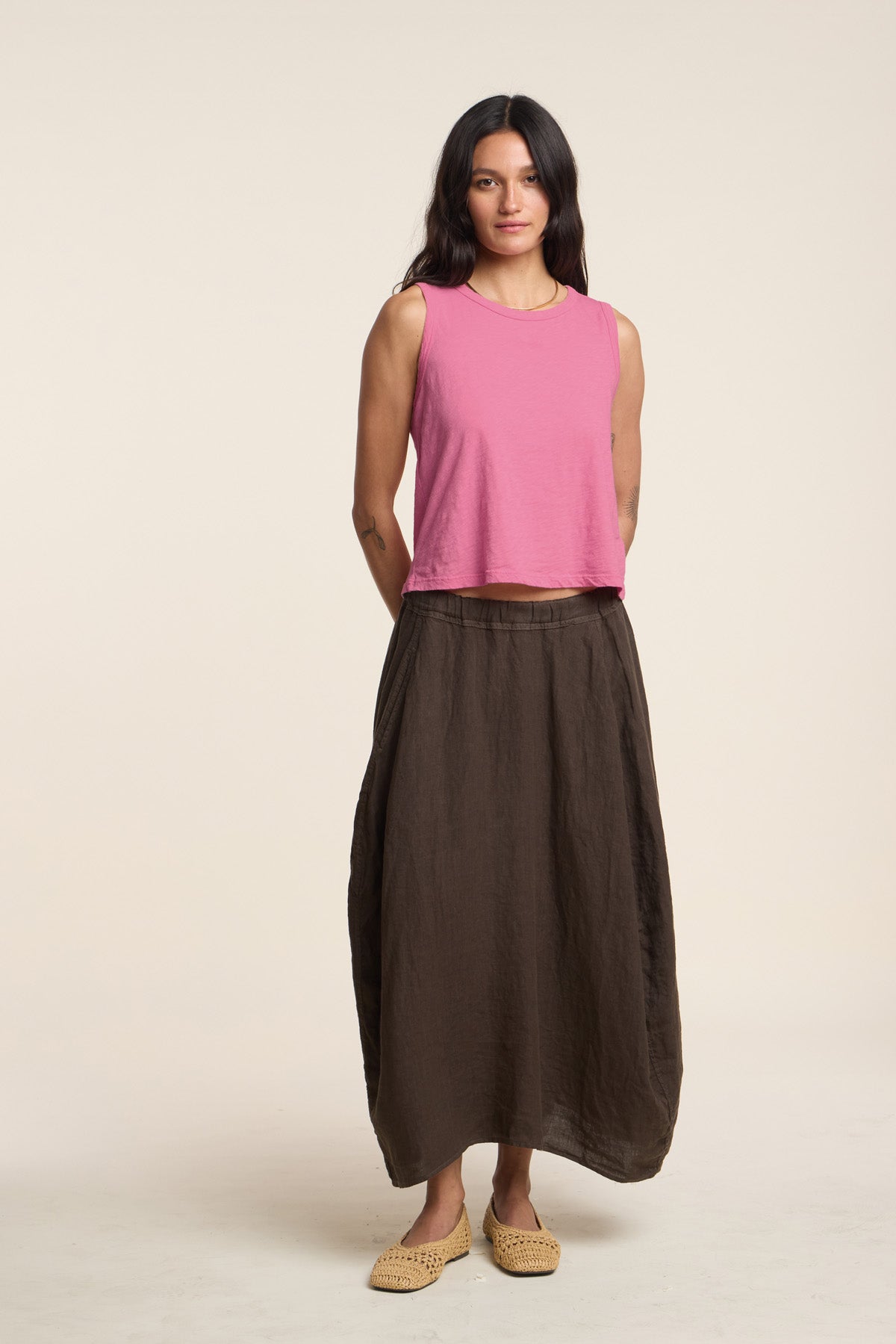 A woman faces forward wearing the AMBRIA TANK TOP by Velvet by Graham & Spencer in sleeveless pink, paired with a long brown skirt and woven beige shoes—an ideal summer look—set against a plain light background.-41387989237953
