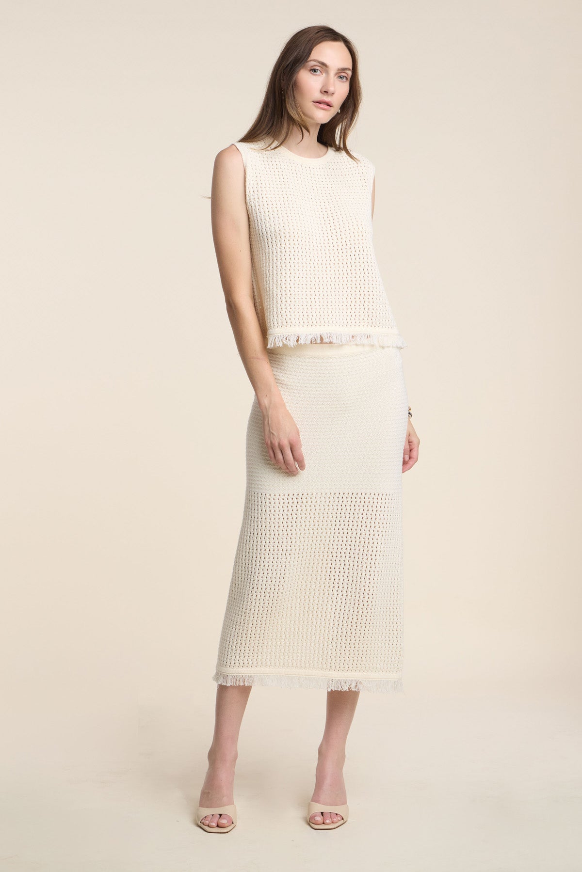 A woman wears the BLYTHE SKIRT by Velvet by Graham & Spencer—a cream cotton mesh pencil skirt with a fringe hem—paired with a matching sleeveless knit top and open-toe heels, set against a neutral background.-41371475968193