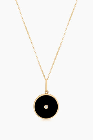 The BALIA BLACK ENAMEL NECKLACE BY THATCH from Thatch features a gold chain and a round black pendant with a small central diamond.