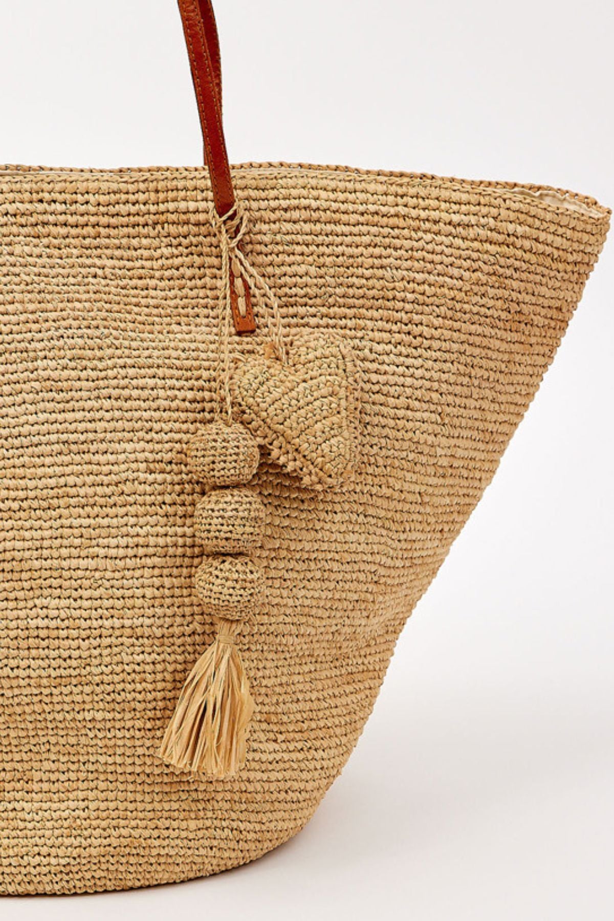 The MARY TOTE by Velvet by Graham & Spencer is a woven straw bag with brown handles, featuring a heart-shaped charm, round beads, and a tassel hanging from one handle.-41323186520257