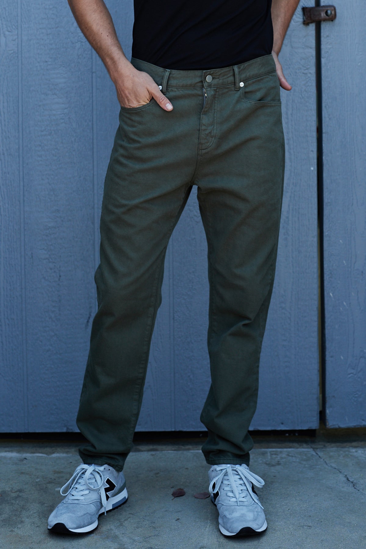 A man is standing in front of a blue door wearing JOSEPH COTTON CANVAS PANTS by Velvet by Graham & Spencer and a black t-shirt.