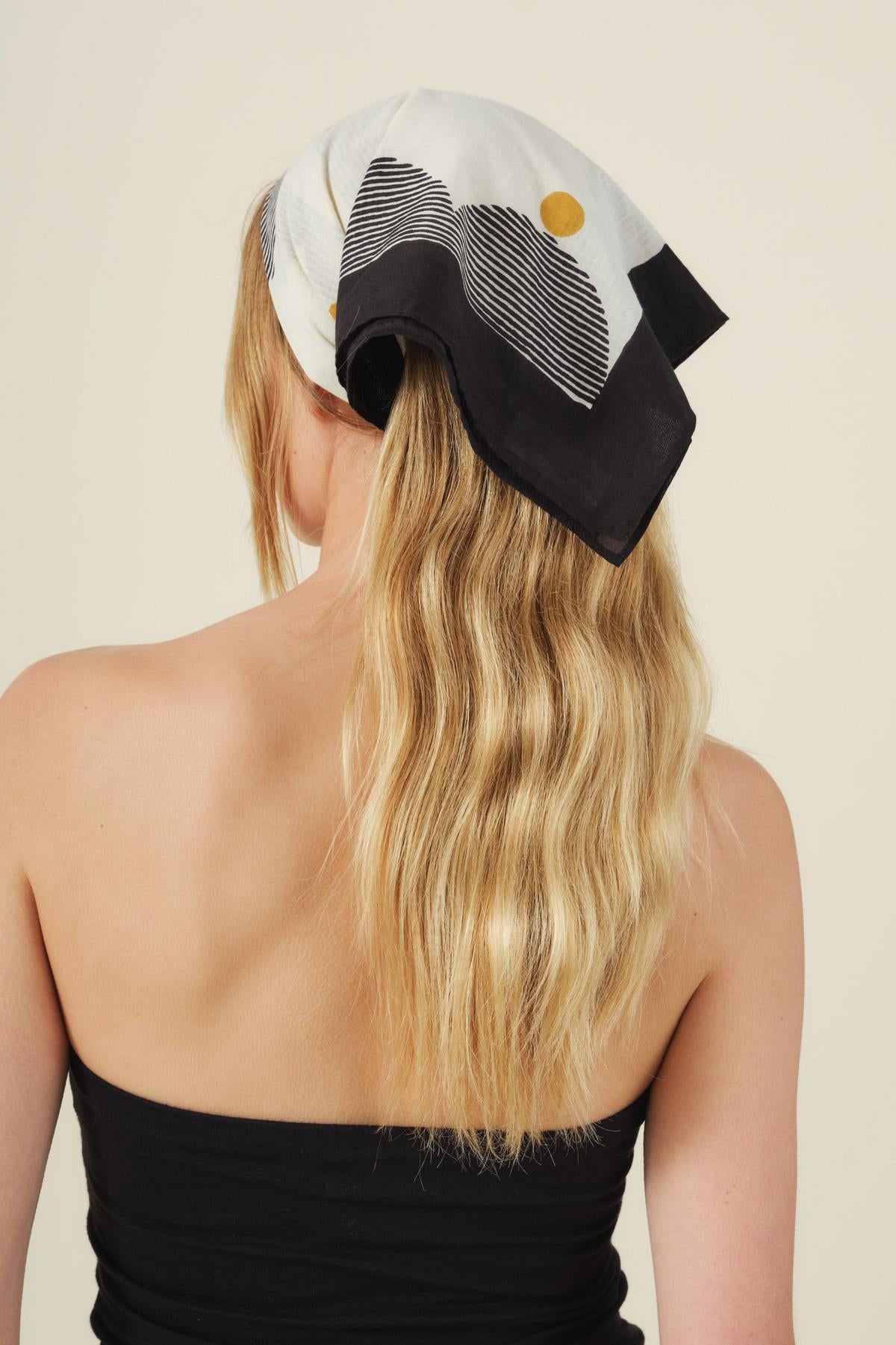 A woman with long, wavy blonde hair wears the ZURI SCARF by Velvet by Graham & Spencer over her head and a black strapless top, photographed from behind against a neutral background.-41455188902081