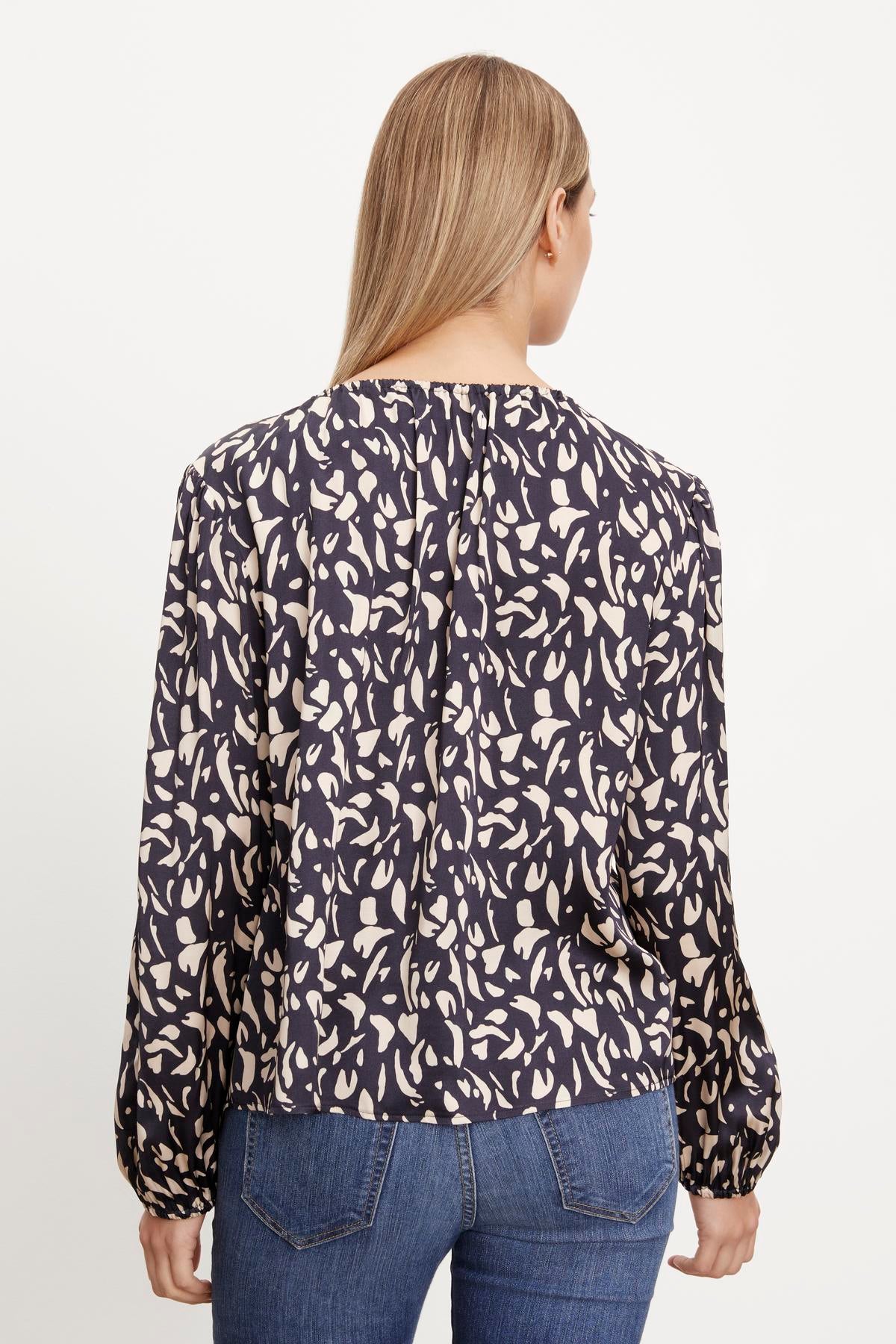 The back view of a woman wearing jeans and a Velvet by Graham & Spencer KADE PRINTED PEASANT BLOUSE with a floral print.-36094326046913