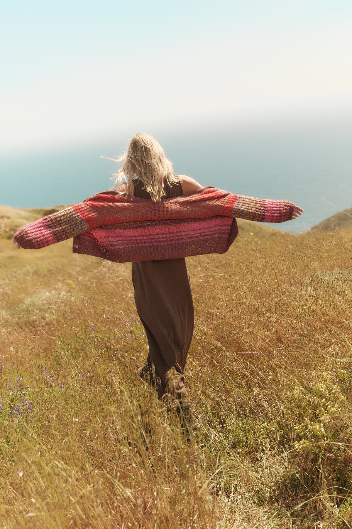 A woman is standing in a field wearing the EDDIE STRIPED CARDIGAN by Velvet by Graham & Spencer.-35701775073473