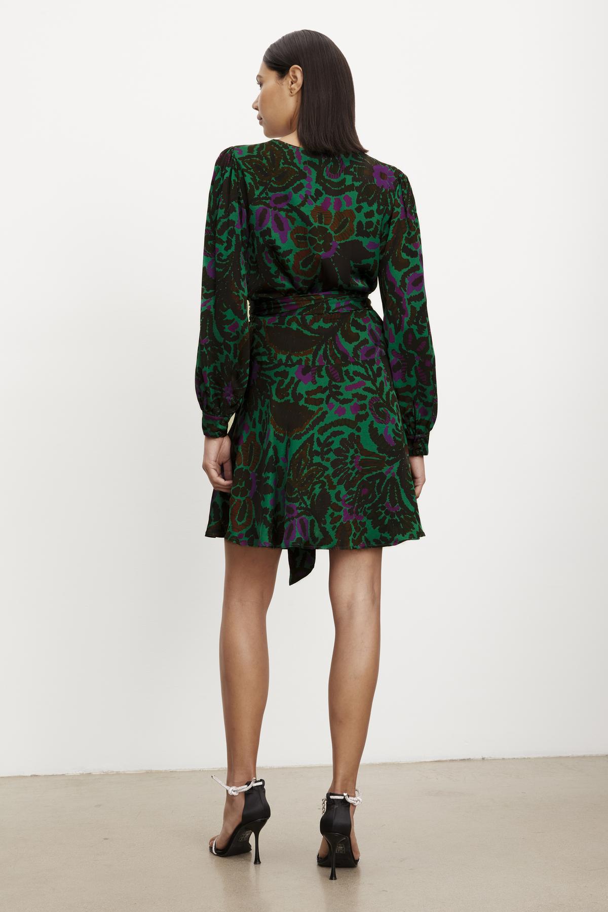 The back view of a woman wearing a Velvet by Graham & Spencer BRIDGET PRINTED SATIN WRAP DRESS with an adjustable tie waist.-35655261782209