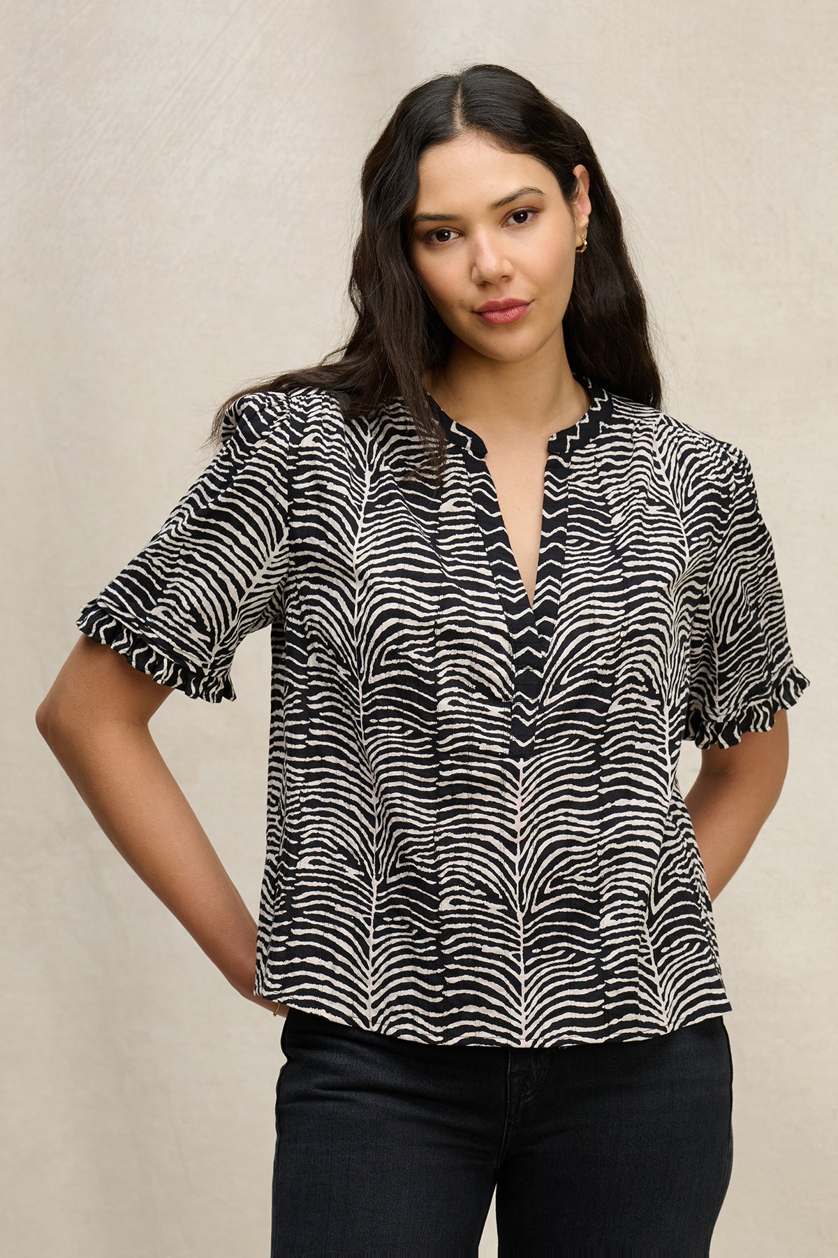 A woman stands facing forward, wearing the FREEDA TOP by Velvet by Graham & Spencer—a black and white patterned cotton top with subtle ruffle short sleeves—and black pants, set against a neutral background.