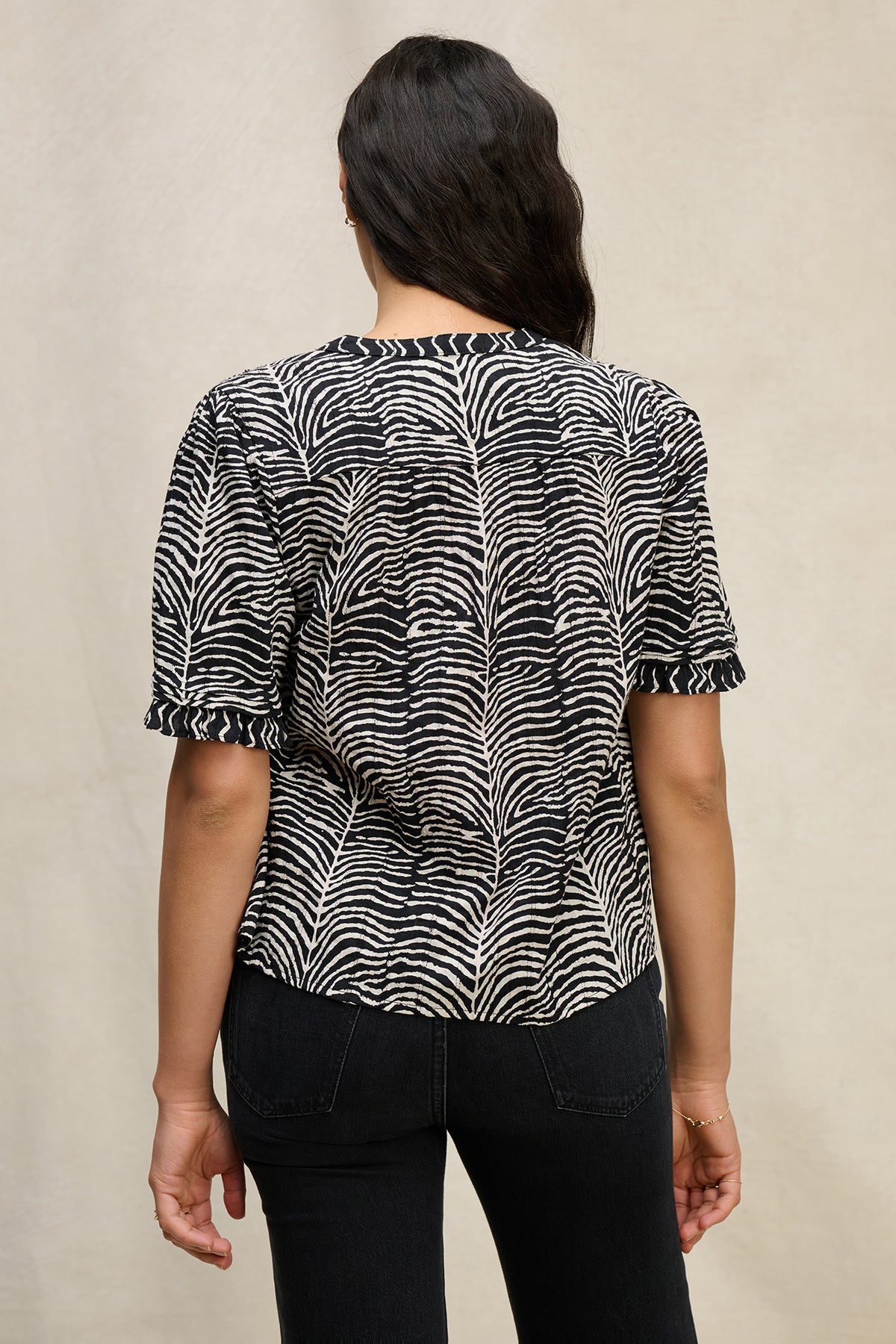A person shown from the back wears the FREEDA TOP by Velvet by Graham & Spencer—a black and white zebra-striped cotton V-neck top—paired with black jeans against a neutral background.