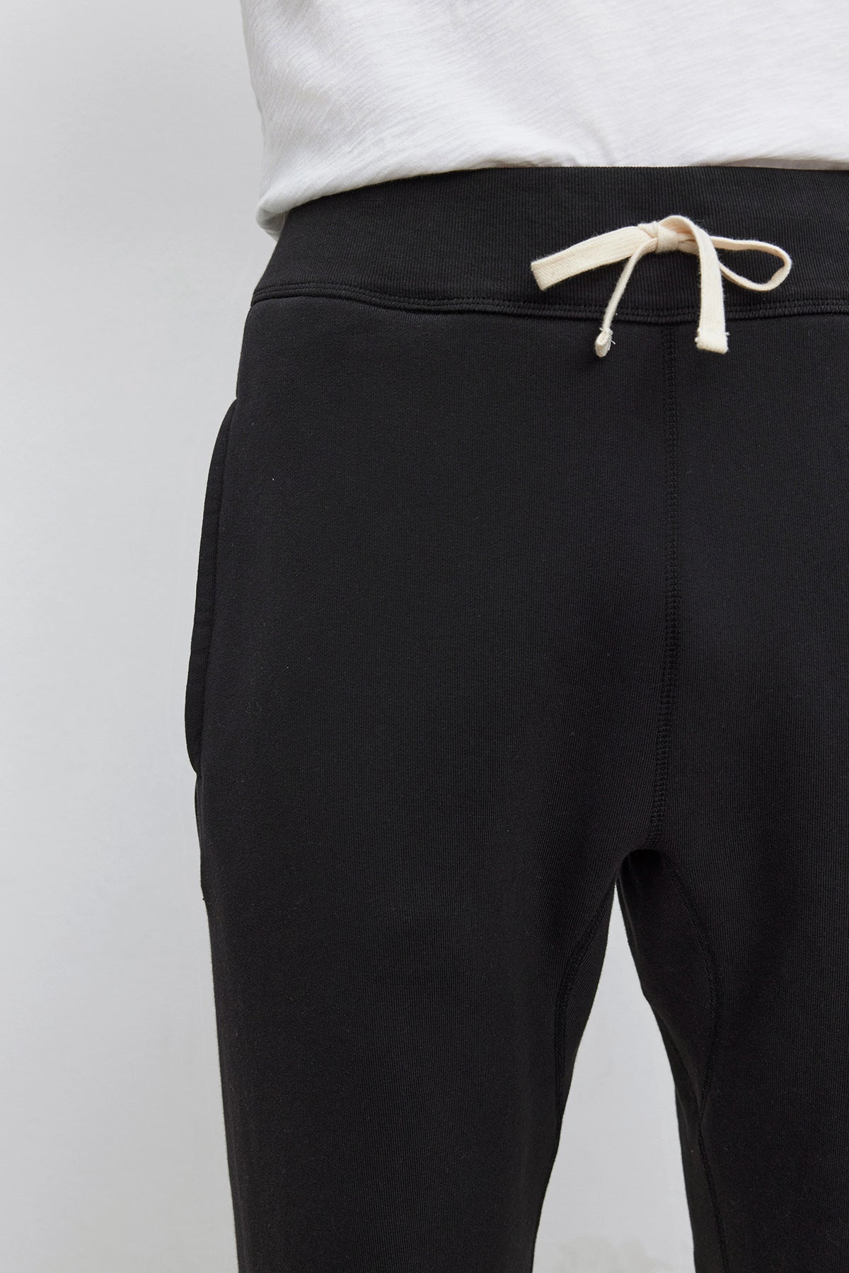 Person wearing KENJI SWEATPANT by Velvet by Graham & Spencer in black with white drawstrings and a white t-shirt, showcasing a comfortable fit.
