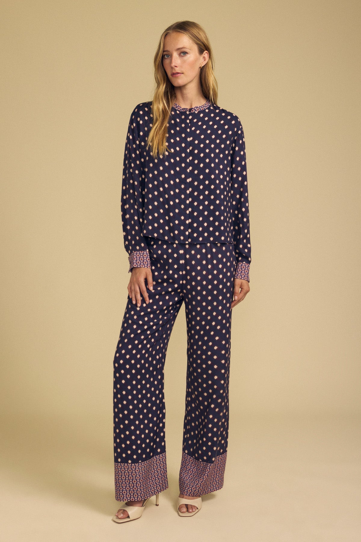 A woman wears a long-sleeved button-down shirt and matching navy blue diamond print CAROL PRINTED PANT by Velvet by Graham & Spencer, both featuring patterned cuffs and hems.-46488190156993