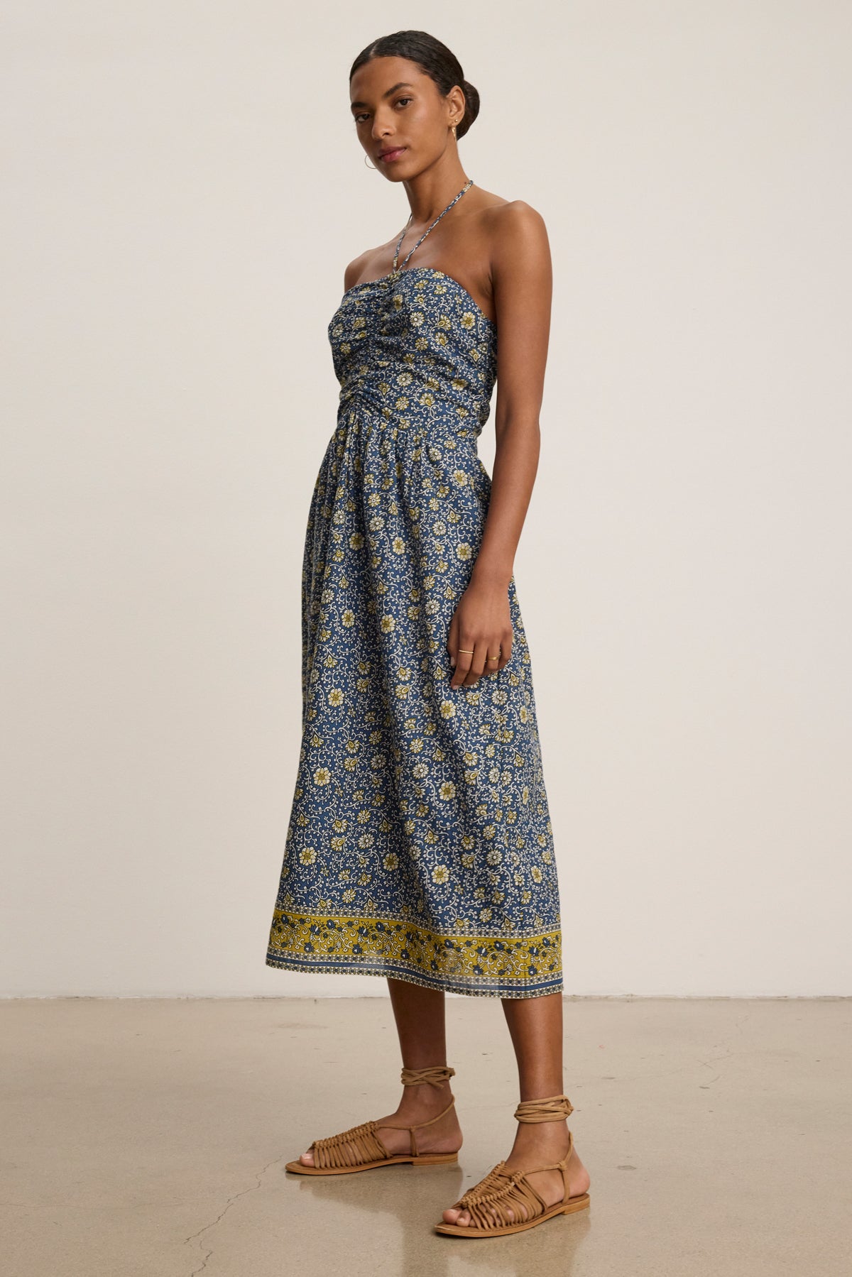 A woman stands indoors in the ODETTE DRESS by Velvet by Graham & Spencer—a chic blue and yellow block print cotton midi dress—paired with sandals, against a plain background.-39333492916417