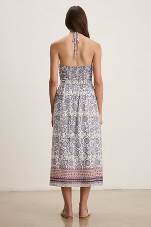 A woman faces away in the Velvet by Graham & Spencer ODETTE DRESS—a chic, ankle-length halter dress in blue and white floral block print cotton—paired with flat sandals.