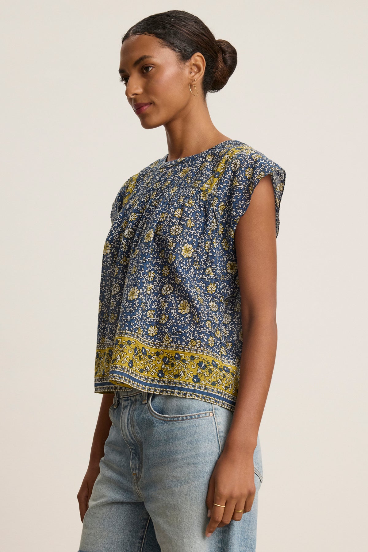 A woman wears the SELENE TOP by Velvet by Graham & Spencer, a chic blue and yellow block print sleeveless blouse, paired with light blue jeans against a plain light background.