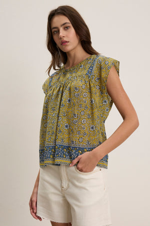 A woman models the Velvet by Graham & Spencer SELENE TOP, a chic yellow and blue block print sleeveless style, paired with off-white shorts against a simple light backdrop.