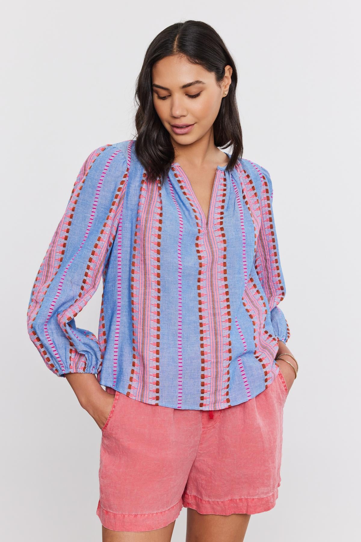 A woman in an ISLA TOP from Velvet by Graham & Spencer, with a v-neckline and coral shorts, standing against a white background.-36910084030657