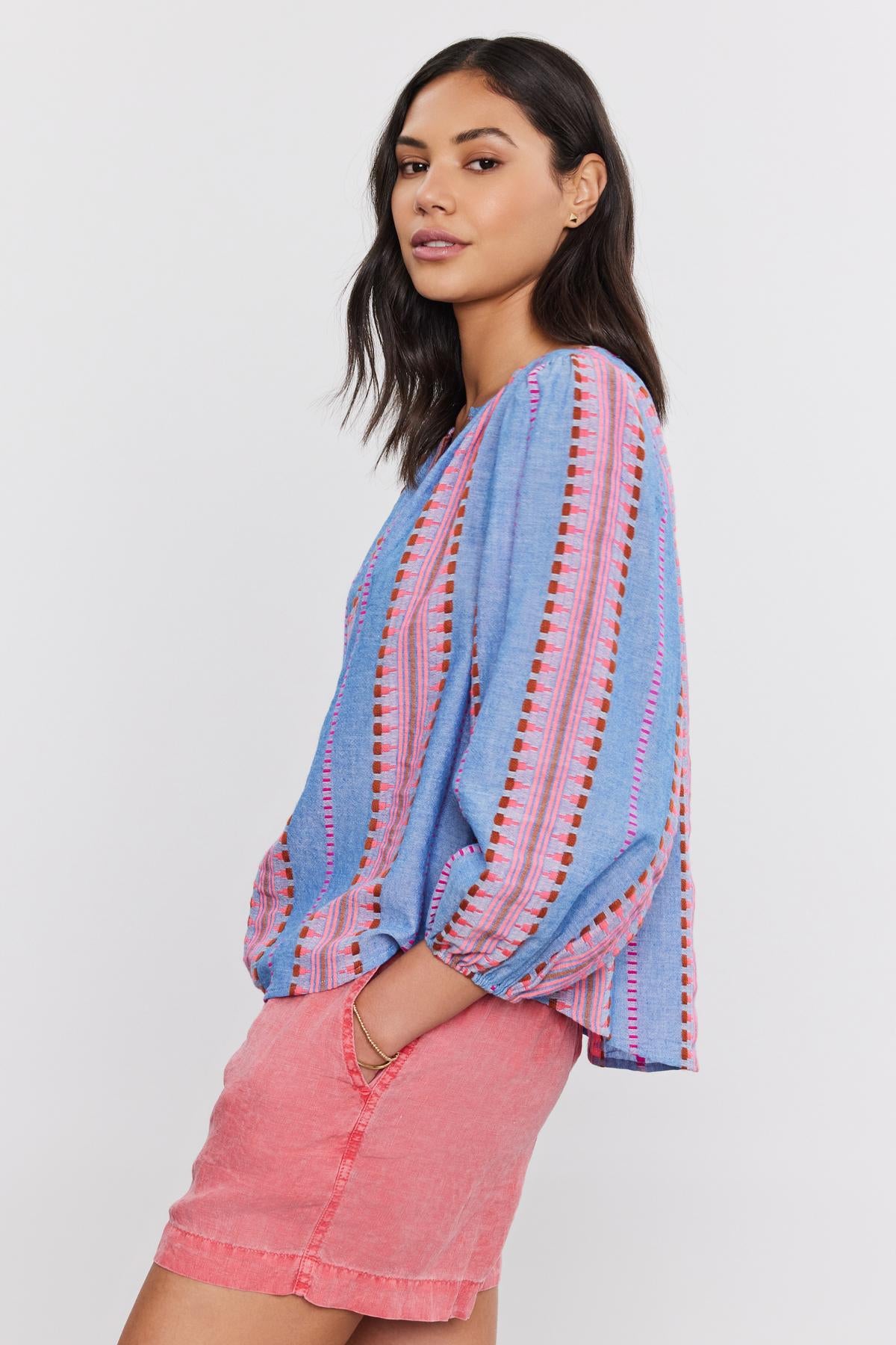 A woman in profile wearing a blue Jacquard stripe fabric ISLA TOP by Velvet by Graham & Spencer and pink shorts, looking over her shoulder.-36910084063425
