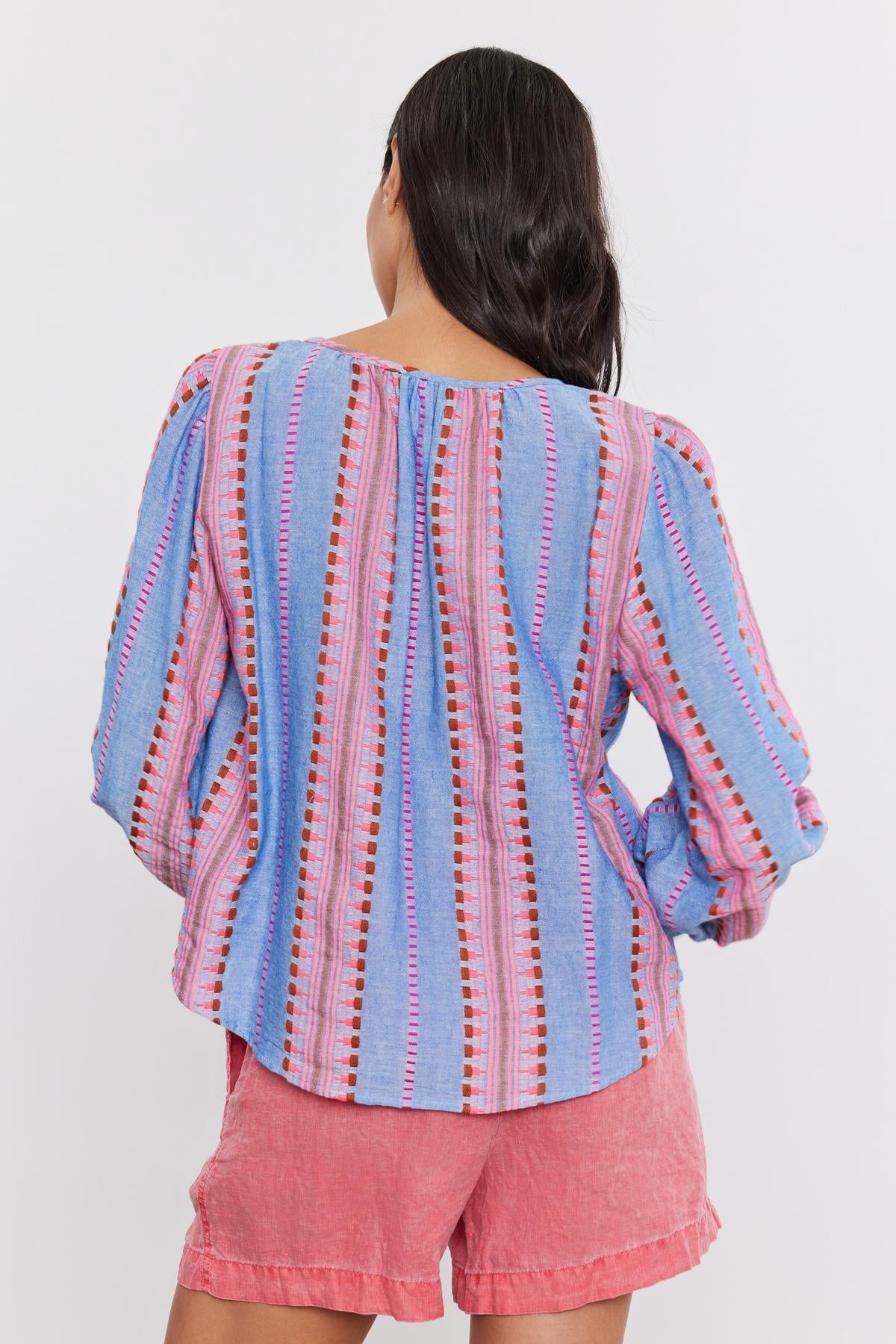 Woman from behind wearing an ISLA TOP by Velvet by Graham & Spencer, a striped blue and pink blouse with a v-neckline, paired with pink shorts, standing in front of a white background.-36910084096193