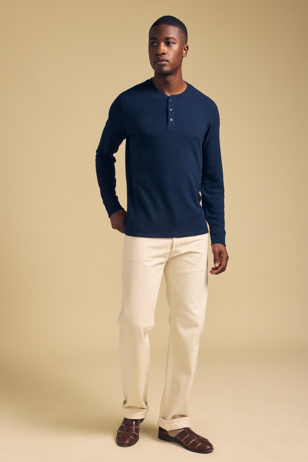 A man wearing a navy blue Velvet by Graham & Spencer ROEN THERMAL HENLEY, cream trousers, and dark brown leather sandals.-46288506192065