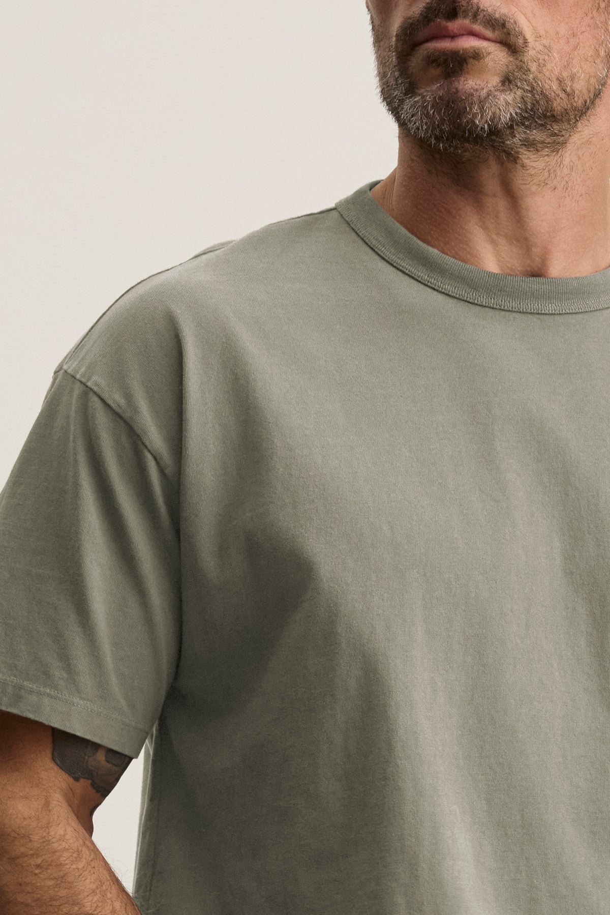 A bearded man wears the versatile BRYAN TEE in plain gray, showcasing its relaxed fit from Velvet by Graham & Spencer.-39018204889281