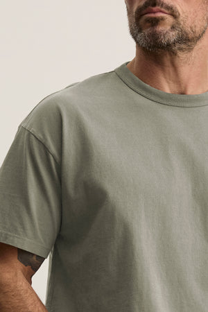 A bearded man wears the versatile BRYAN TEE in plain gray, showcasing its relaxed fit from Velvet by Graham & Spencer.