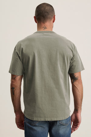 A man in a relaxed fit BRYAN TEE by Velvet by Graham & Spencer and jeans, viewed from behind. His shaved head and tattoos on his arms and neck effortlessly reflect everyday versatility.
