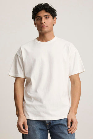 Person wearing a plain white BRYAN TEE from Velvet by Graham & Spencer, crafted from soft pima cotton jersey, paired with blue jeans against a neutral background. The relaxed fit offers everyday versatility, effortlessly blending style and comfort.