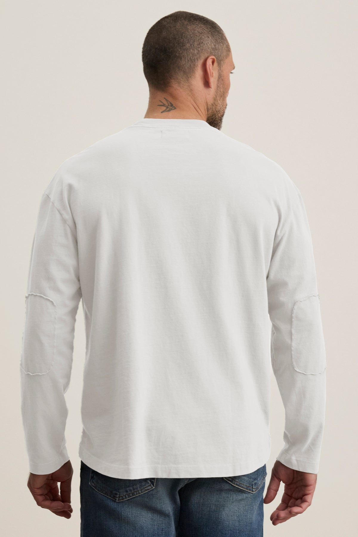 A person with a short haircut is seen from the back wearing the BRYAN TEE, a plain white long-sleeve shirt by Velvet by Graham & Spencer, made from structured pima cotton and paired with relaxed fit jeans for everyday versatility.-39018195386561
