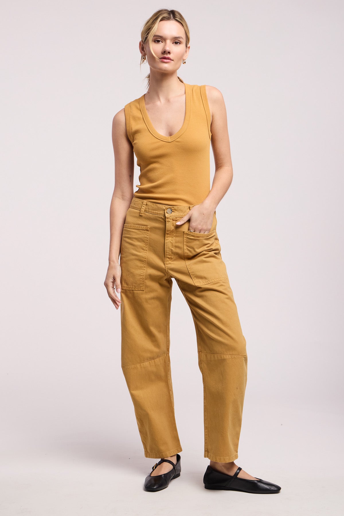 A woman stands against a plain background wearing a sleeveless tan top, black flats, and the BRYLIE PANT by Velvet by Graham & Spencer—cotton twill barrel-leg pants featuring utilitarian patch pockets.-41374540431553