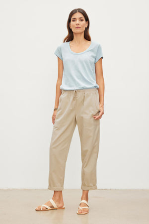 The model is wearing a blue t-shirt and Velvet by Graham & Spencer khaki pants. The MISTY COTTON TWILL PANT has an elastic waist and drawstring, providing comfort and adjustability.