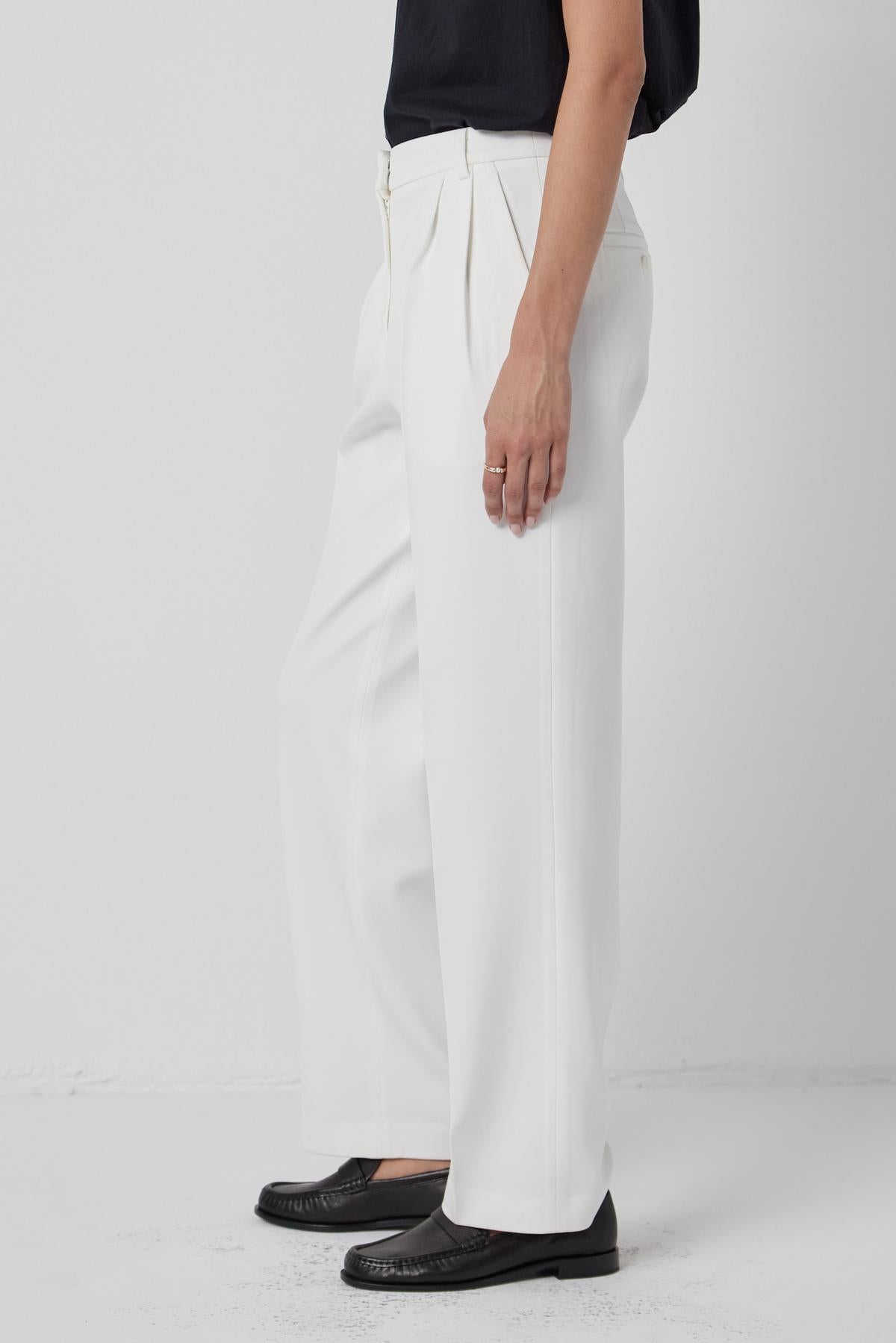 A woman wearing white Bundy Pants and a black top, wardrobe staple by Velvet by Jenny Graham.-36168659108033