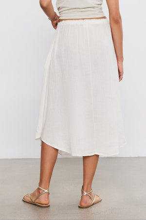 Woman from behind wearing a Velvet by Graham & Spencer Nemy Linen Skirt with thin straps and flat sandals on a plain background for a casual daytime look.