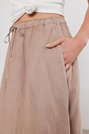 Close-up of a person wearing a Velvet by Graham & Spencer NEMY LINEN SKIRT with an elastic waist, hand casually placed in the pocket.