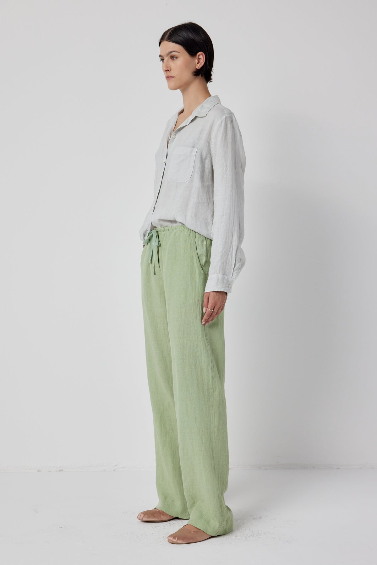 Woman standing in a studio, wearing a casual white shirt and light green Velvet by Jenny Graham Pico Linen Pant with an elastic waist, looking to the side, with a neutral expression.