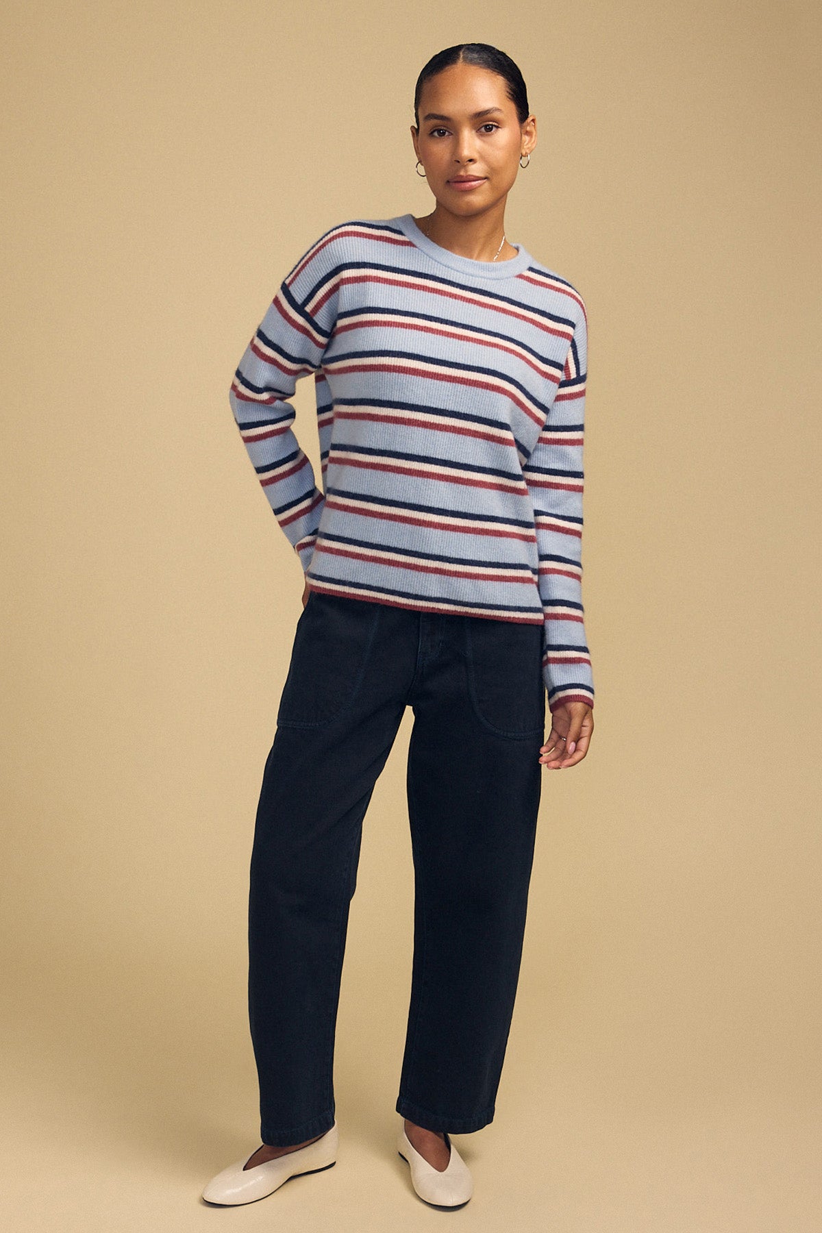 A person wearing the BETH SWEATER, a cozy knit crew neck with horizontal red, navy, and white stripes, paired with dark trousers and light-colored slip-on shoes.-46488108695745