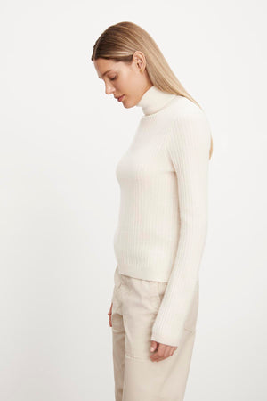 The model is wearing a white LORI CASHMERE TURTLENECK SWEATER by Velvet by Graham & Spencer and beige pants.