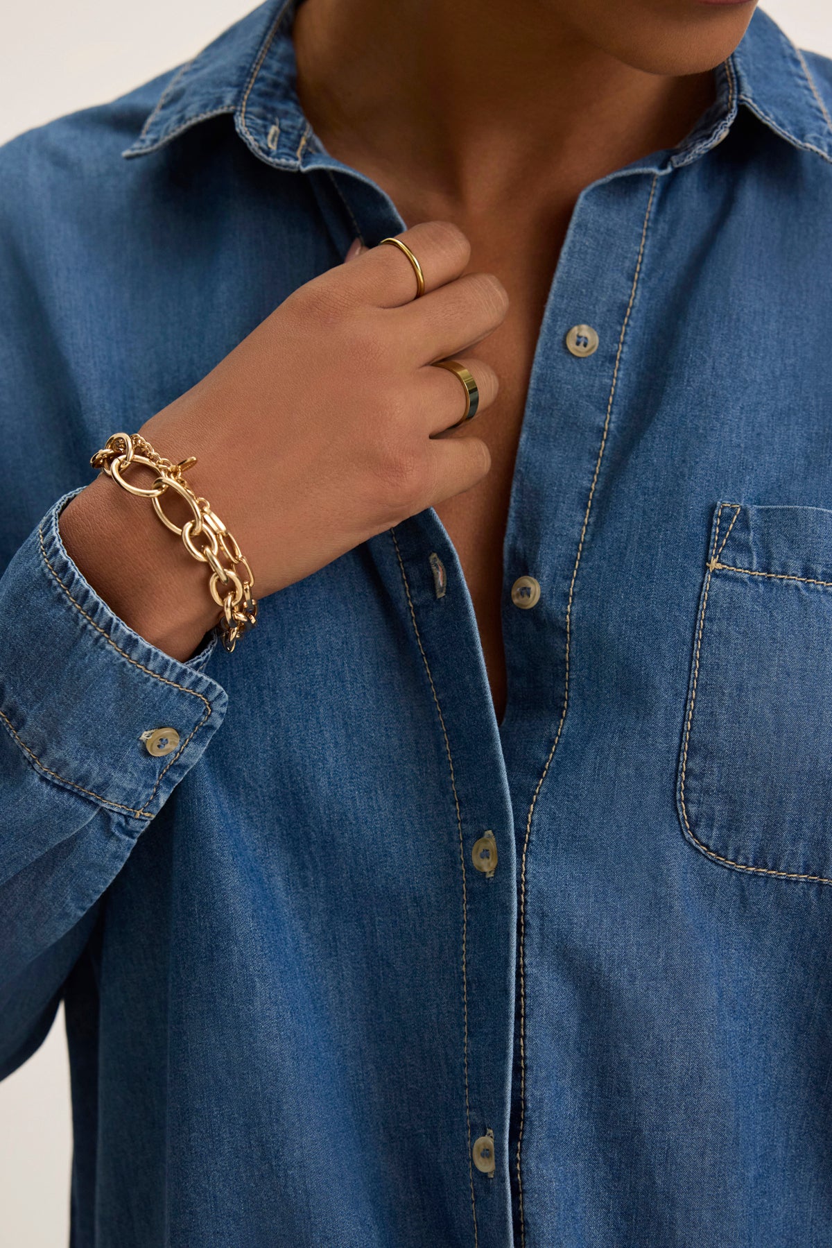 Wearing the KASSA CHAMBRAY SHIRT by Velvet by Graham & Spencer, accessorizing with gold rings and a chain bracelet on their left hand, exudes a timeless look.-38820662051009