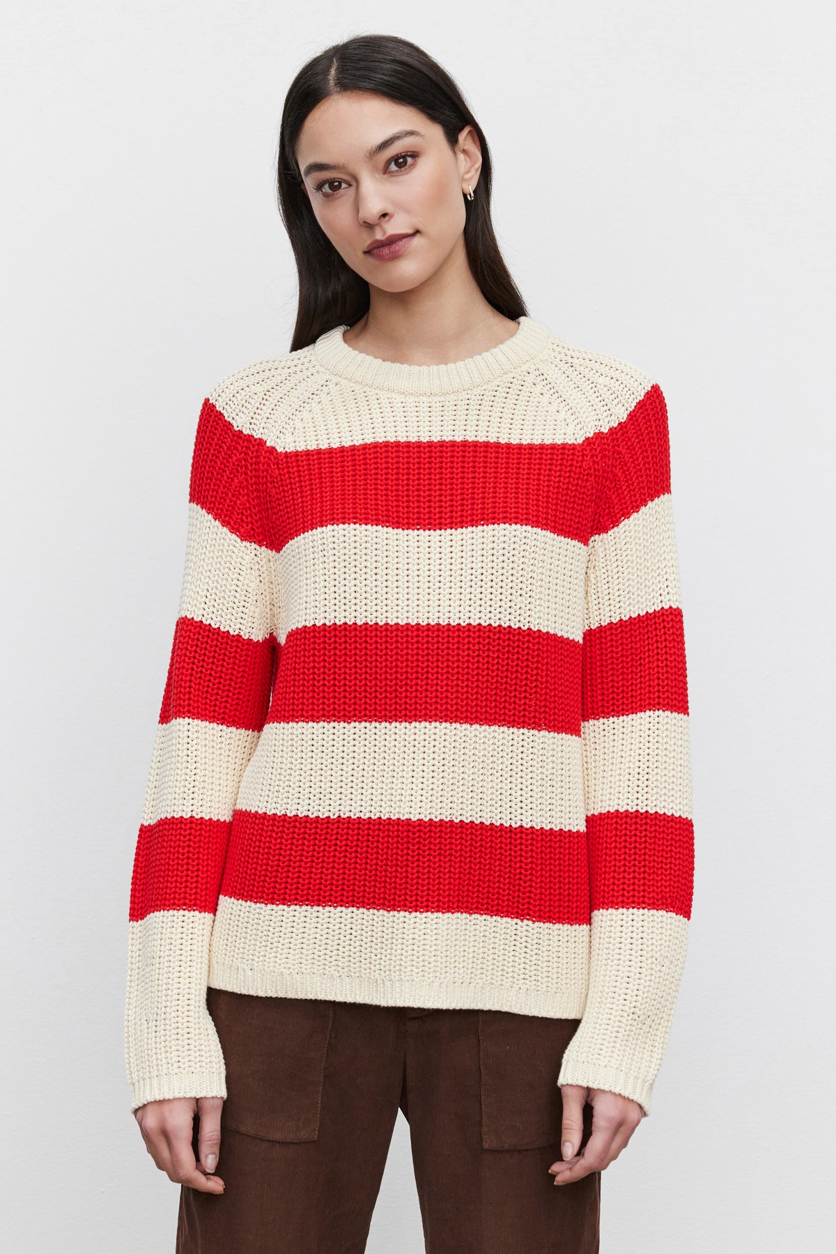 A person wearing the CIARA SWEATER from Velvet by Graham & Spencer, featuring cream and red horizontal stripes in a cotton knit fabric, is paired with brown pants and stands against a plain white background.-37665553612993