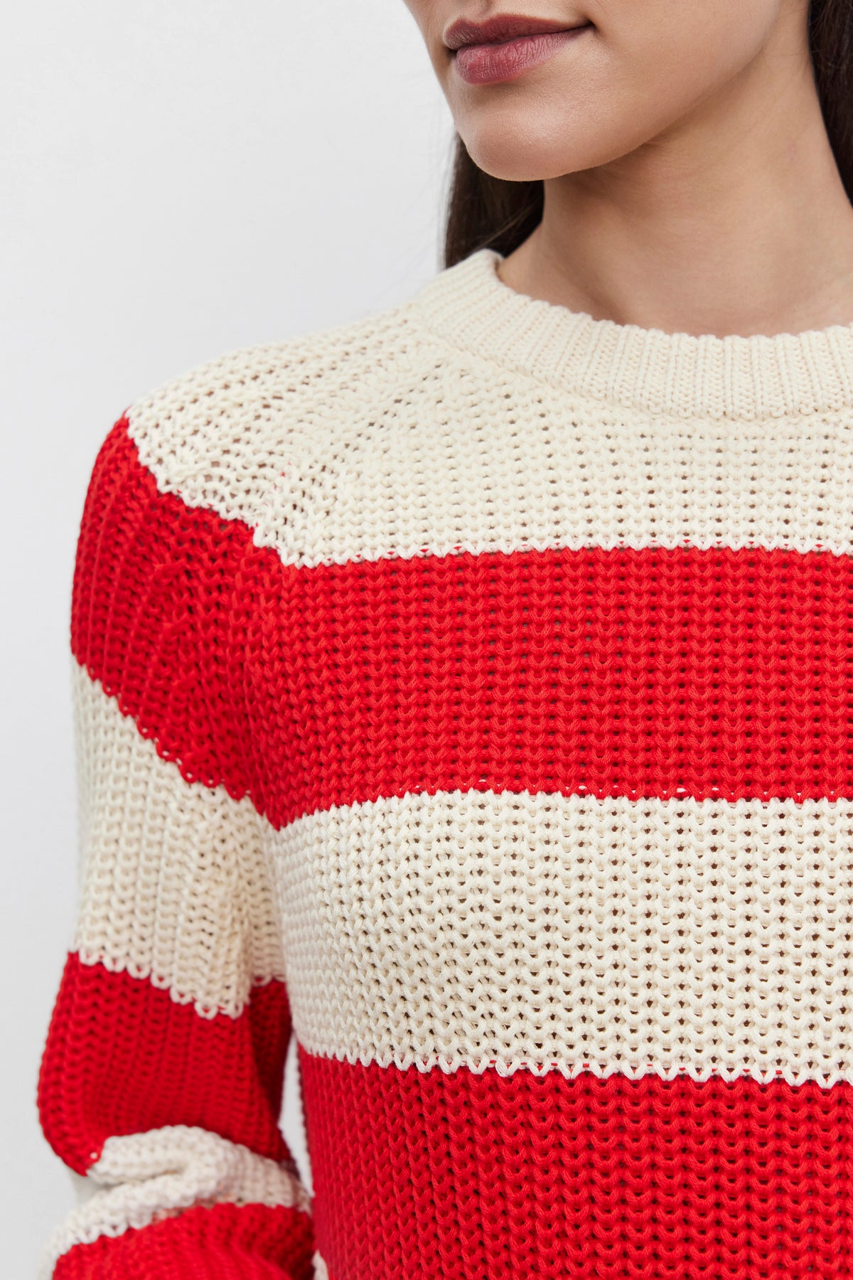 A close-up of a person wearing the CIARA SWEATER by Velvet by Graham & Spencer, featuring a cotton knit design with alternating red and cream horizontal stripes. The striped pattern highlights the upper torso and shoulder area, while the face remains partially visible.-37665553711297