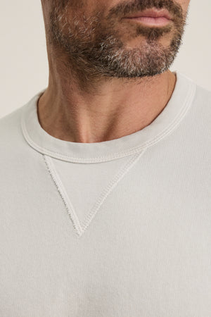 Close-up of a man's lower face and neck wearing the CILLIAN SWEATSHIRT by Velvet by Graham & Spencer, a vintage-inspired, light-colored crewneck with visible stitching detail near the collar.