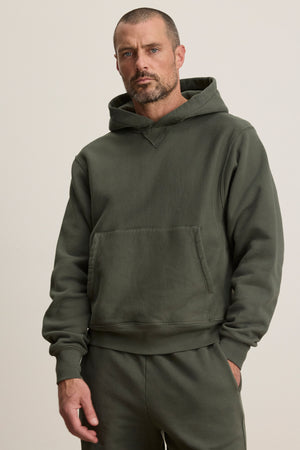 Model wears the KAZ HOODIE by Velvet by Graham & Spencer, an olive green relaxed fit with matching sweatpants and a kangaroo pouch pocket, set against a plain light background.