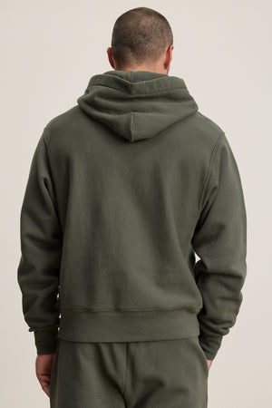 A person is seen from the back wearing the Velvet by Graham & Spencer KAZ HOODIE in olive green with a relaxed fit, kangaroo pouch pocket, and matching pants, set against a plain background.