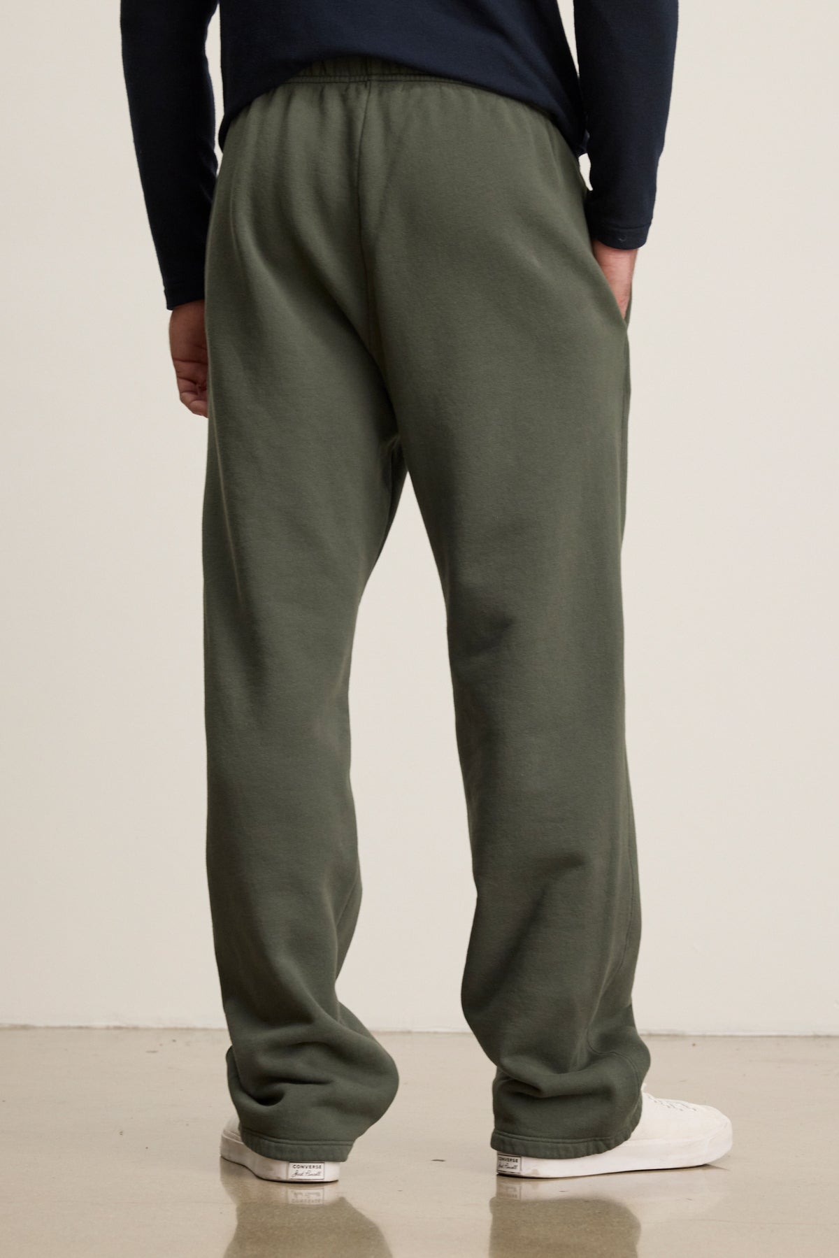 A person stands facing away, wearing Velvet by Graham & Spencer’s HUDSON SWEATPANT in olive green cotton fleece with a dark long-sleeve shirt and white sneakers—an ideal look for everyday wear.
