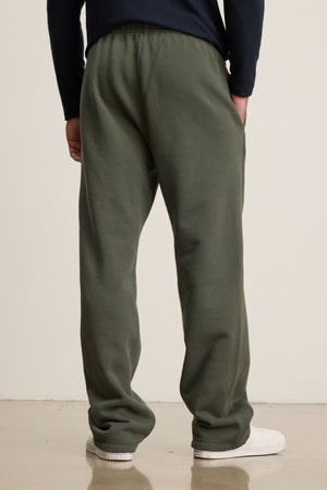 A person stands facing away, wearing Velvet by Graham & Spencer’s HUDSON SWEATPANT in olive green cotton fleece with a dark long-sleeve shirt and white sneakers—an ideal look for everyday wear.