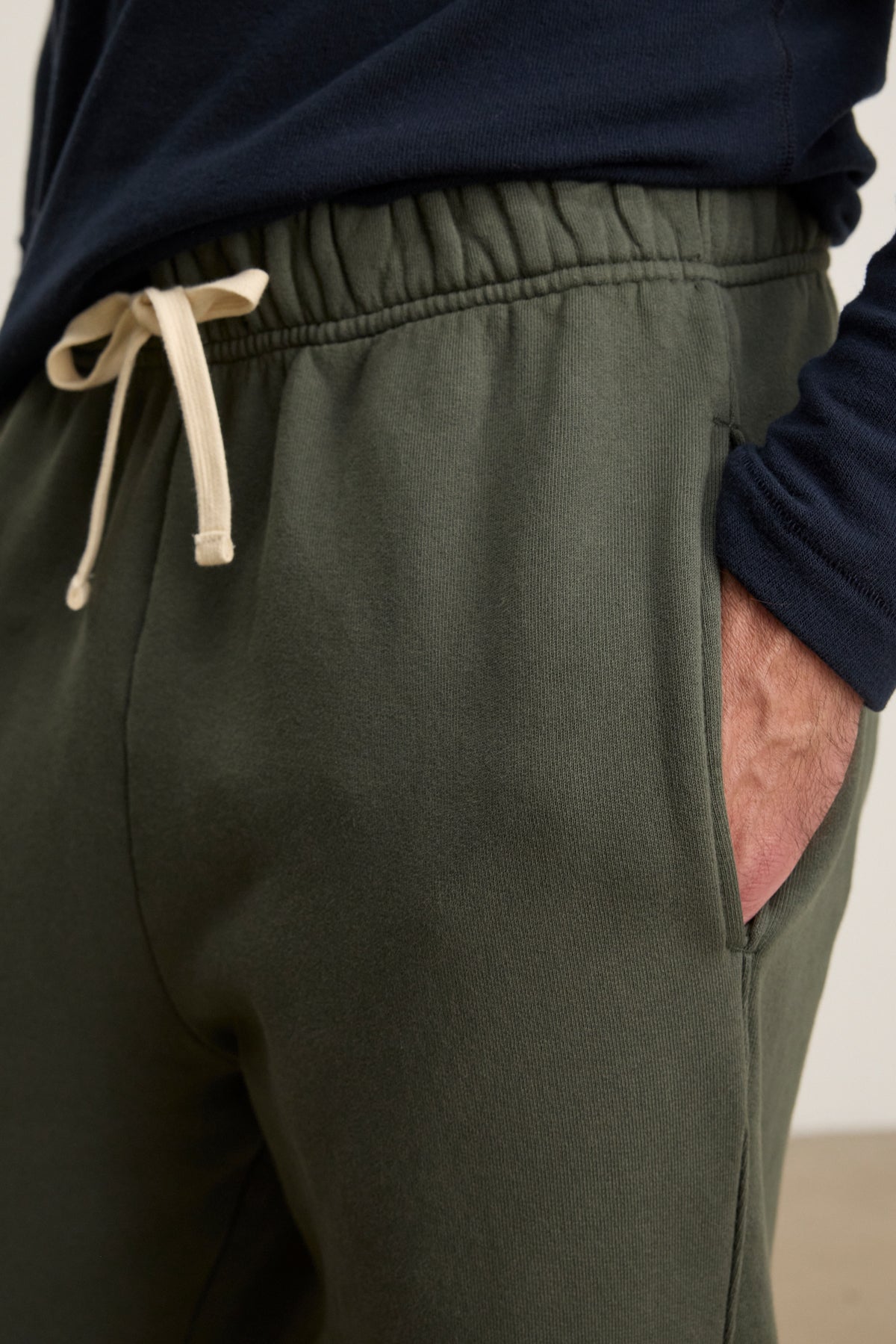 A person wears Velvet by Graham & Spencer's HUDSON SWEATPANT in dark green cotton fleece and a navy blue long-sleeve shirt, one hand in their pocket—an ideal look for everyday wear.
