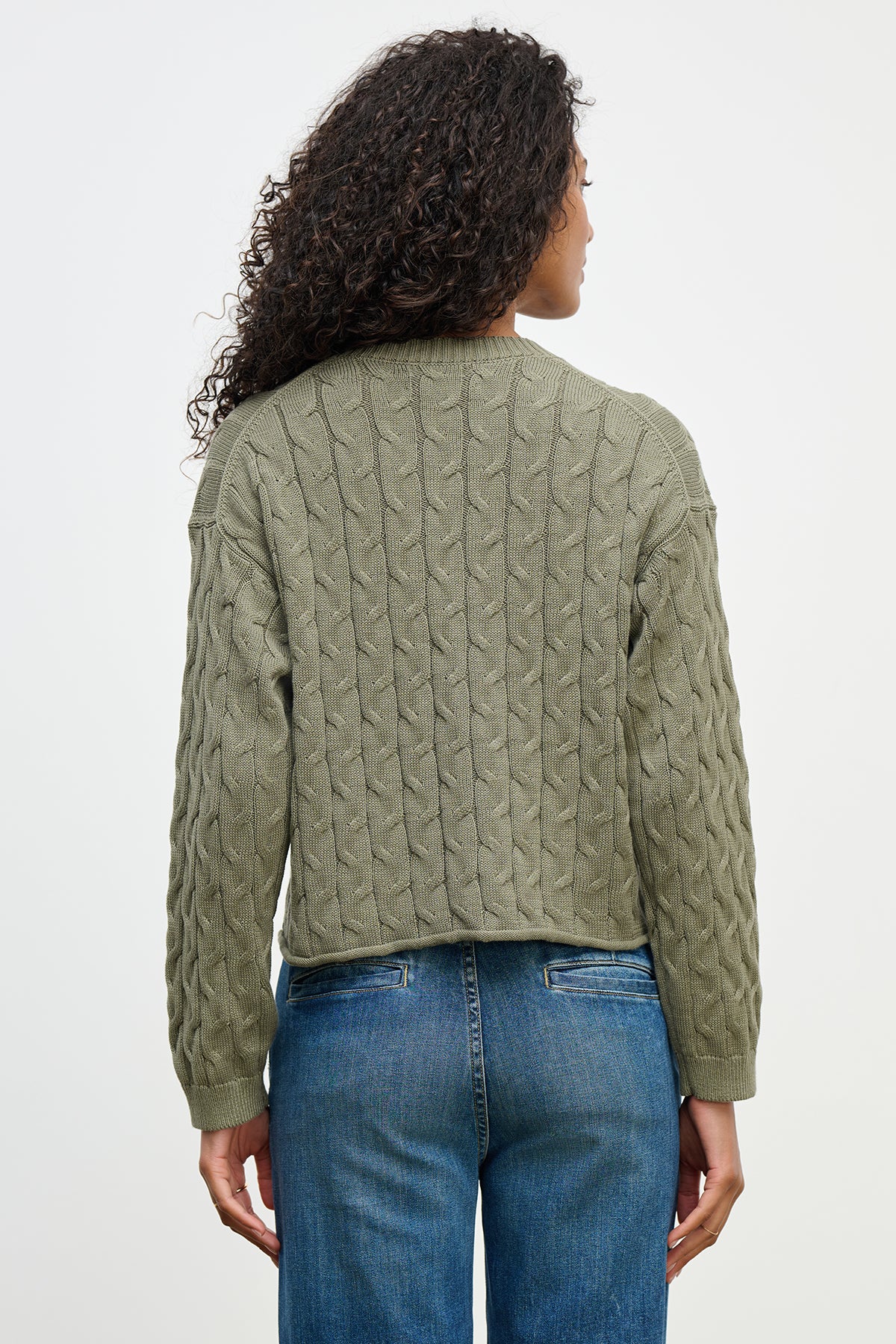 A woman with curly hair is seen from the back wearing a boxy fit olive green APRIL SWEATER by Velvet by Graham & Spencer and blue jeans.-38662829146305