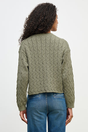 A woman with curly hair is seen from the back wearing a boxy fit olive green APRIL SWEATER by Velvet by Graham & Spencer and blue jeans.