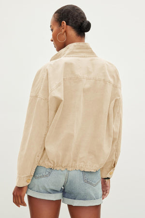 A person with short hair, wearing hoop earrings and a Velvet by Graham & Spencer NICOLA JACKET over denim shorts, stands with their back to the camera against a plain background.