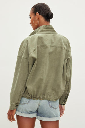 A person with short hair is wearing an olive green NICOLA JACKET by Velvet by Graham & Spencer and blue denim shorts, viewed from the back against a plain background.